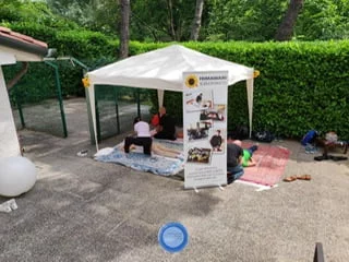 A group of people do Shiatsu treatment under a tent in a courtyard.