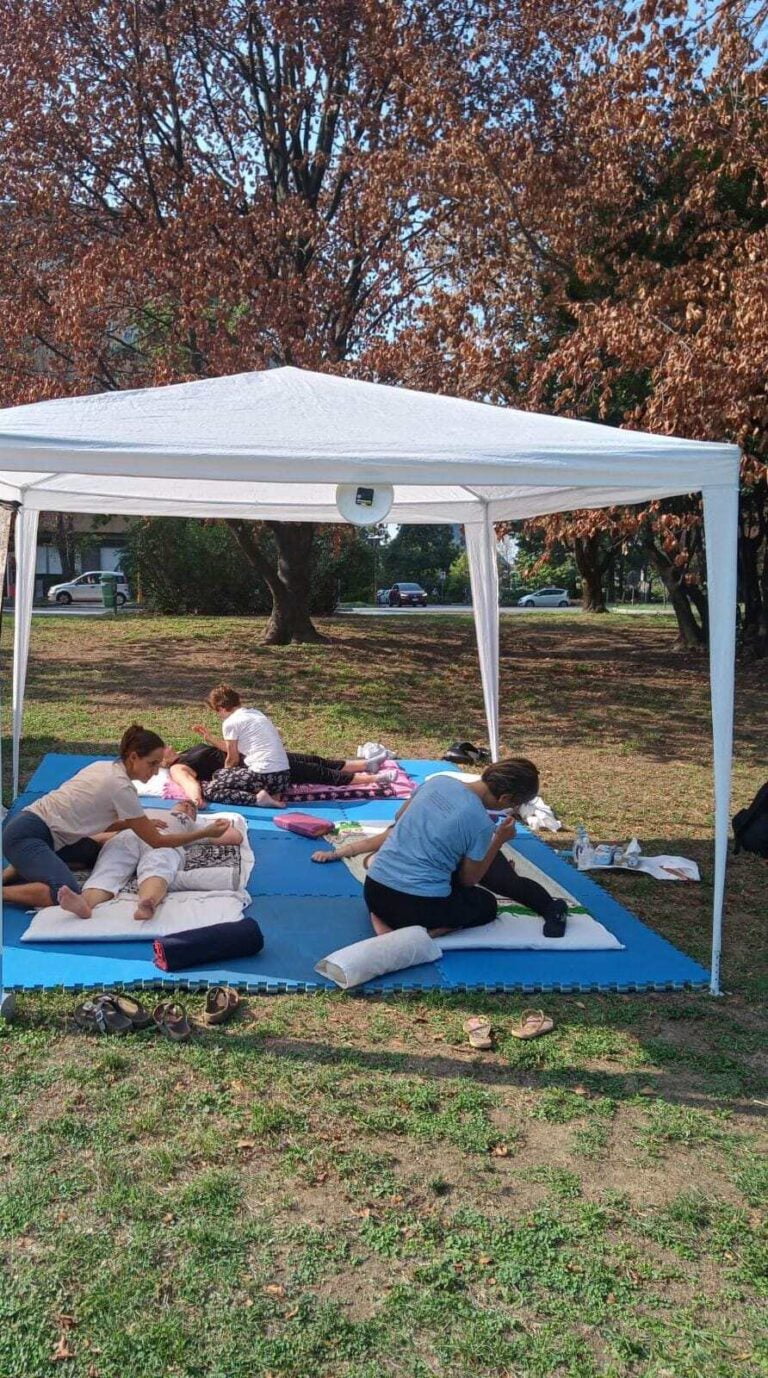 Large white gazebo in a park with three occupied treatment stations on the ground.
